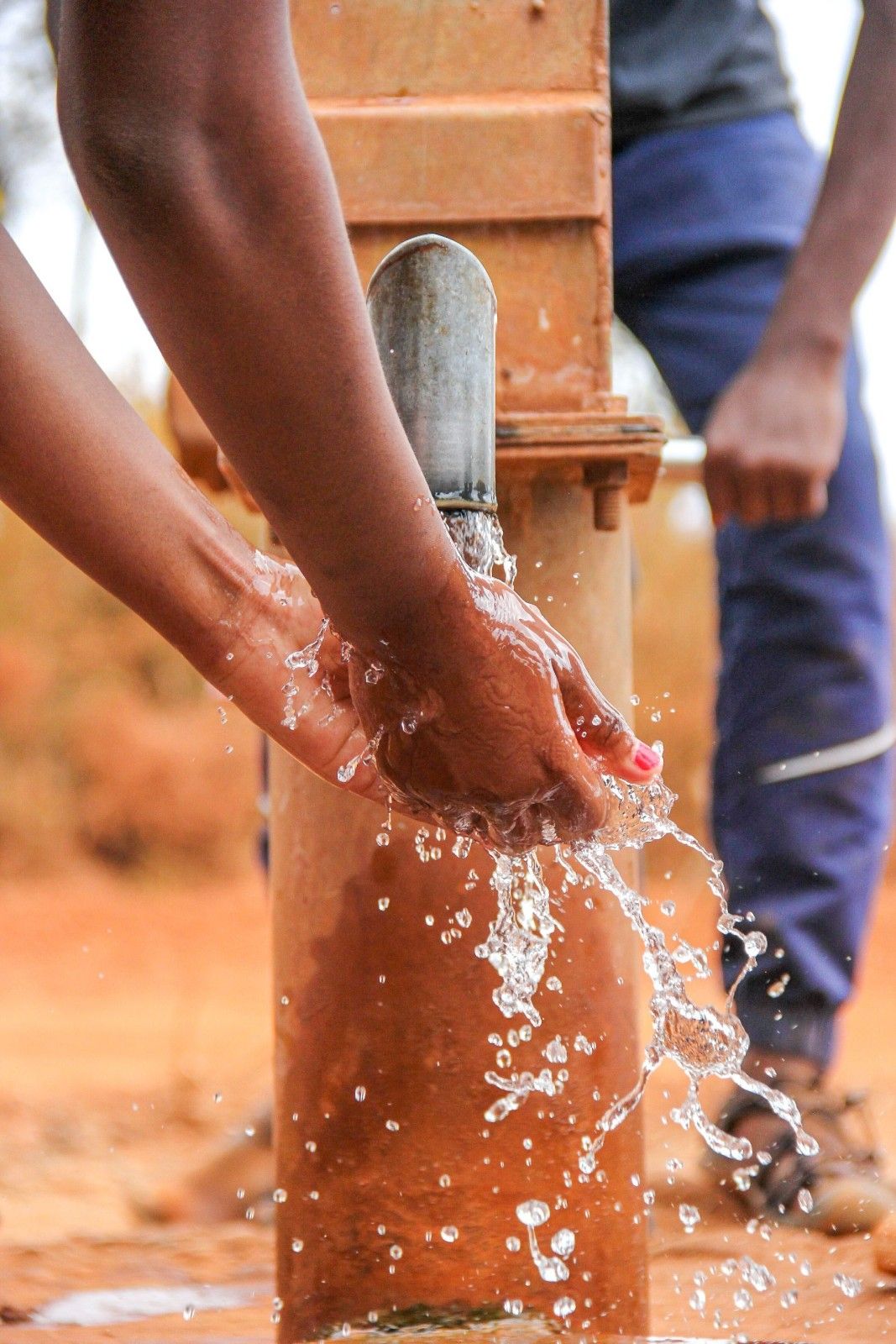 Close-up of hands being washed at a rural water pump outdoors.